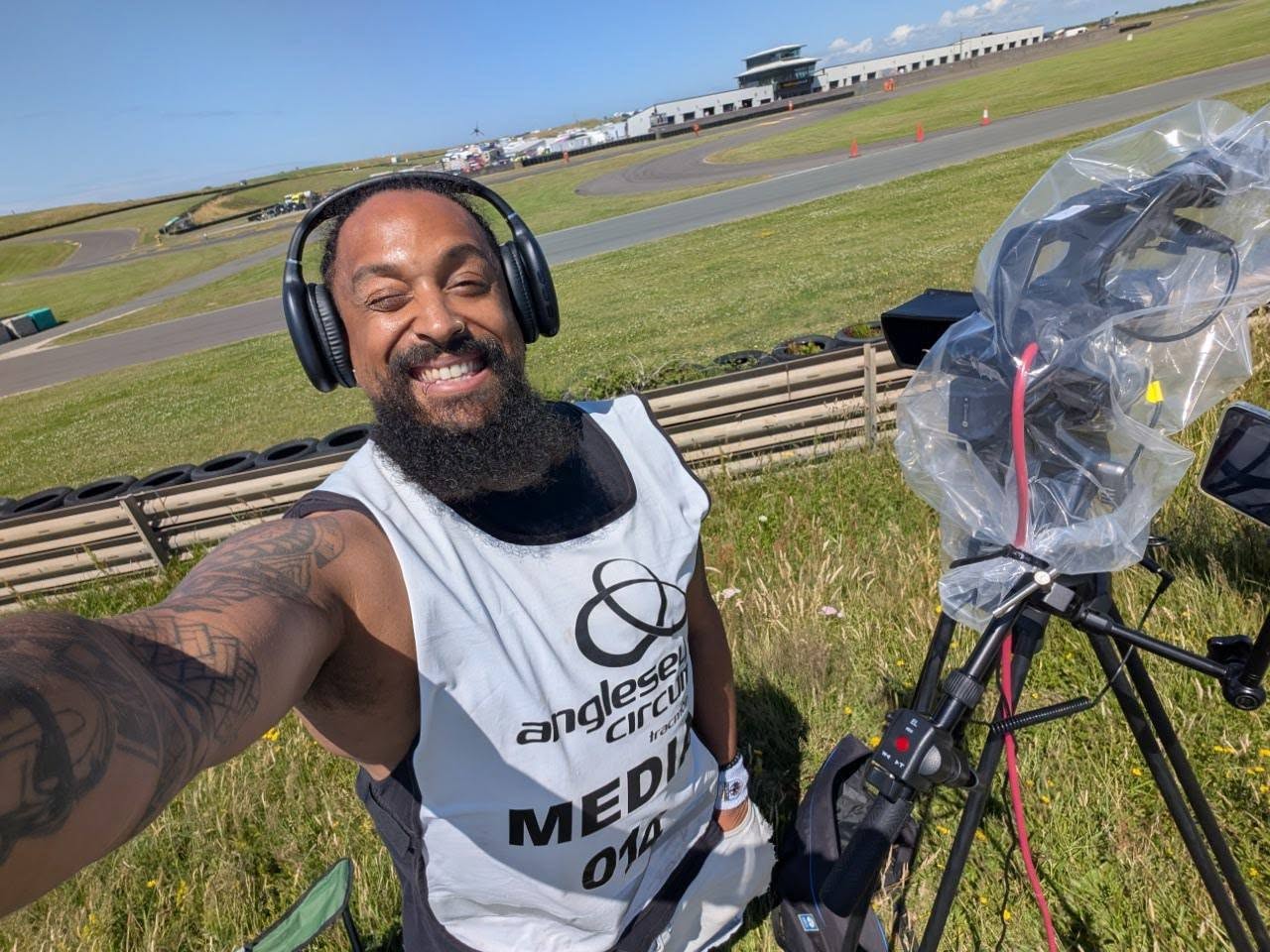 Troy with a camera and headset beside a motor racing circuit